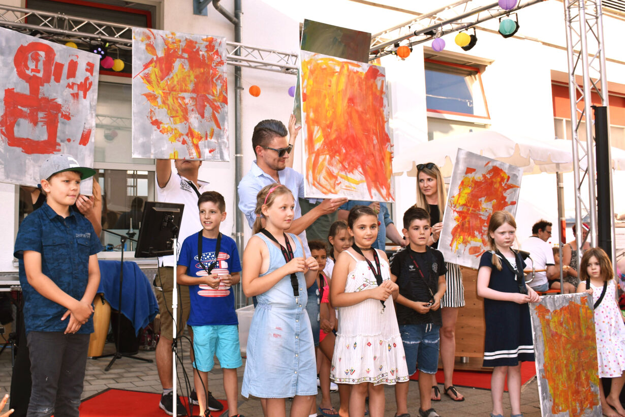 Präsentation der Kunstwerke, die für den guten Zweck versteigert werden. Die jeweiligen Künstler stehen davor.  Sommerfest 2018 Bilder